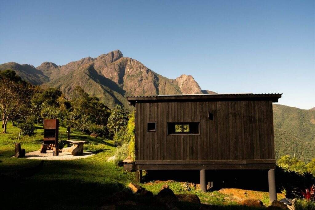 Vista dos fundos da cabana minimalista com pilares de sustentação para preservação a topografia do terreno 
